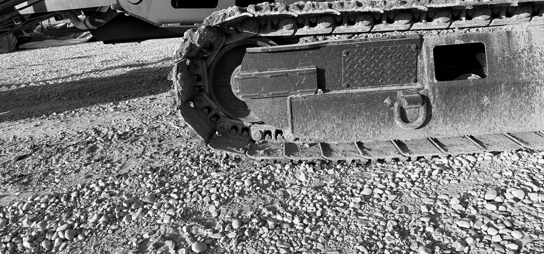 A track chain over its idler on an excavator undercarriage, standing on gravel