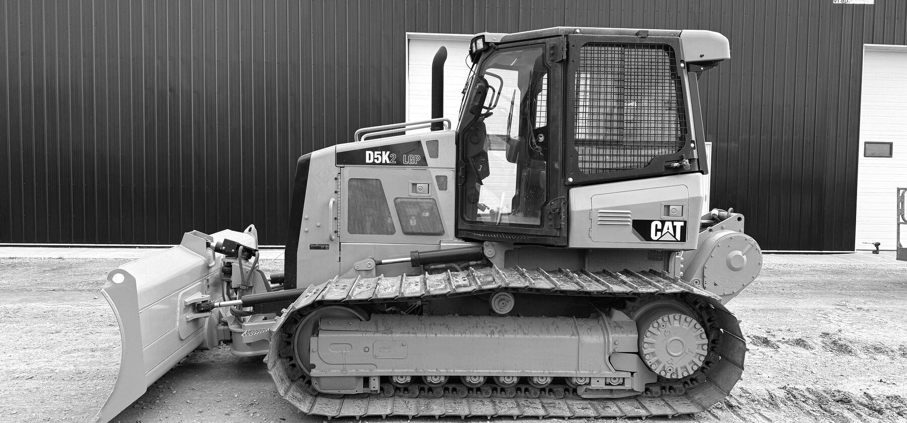 A Cat D5K2 LGP dozer parked in the yard, blade and track in profile against a dark shop wall