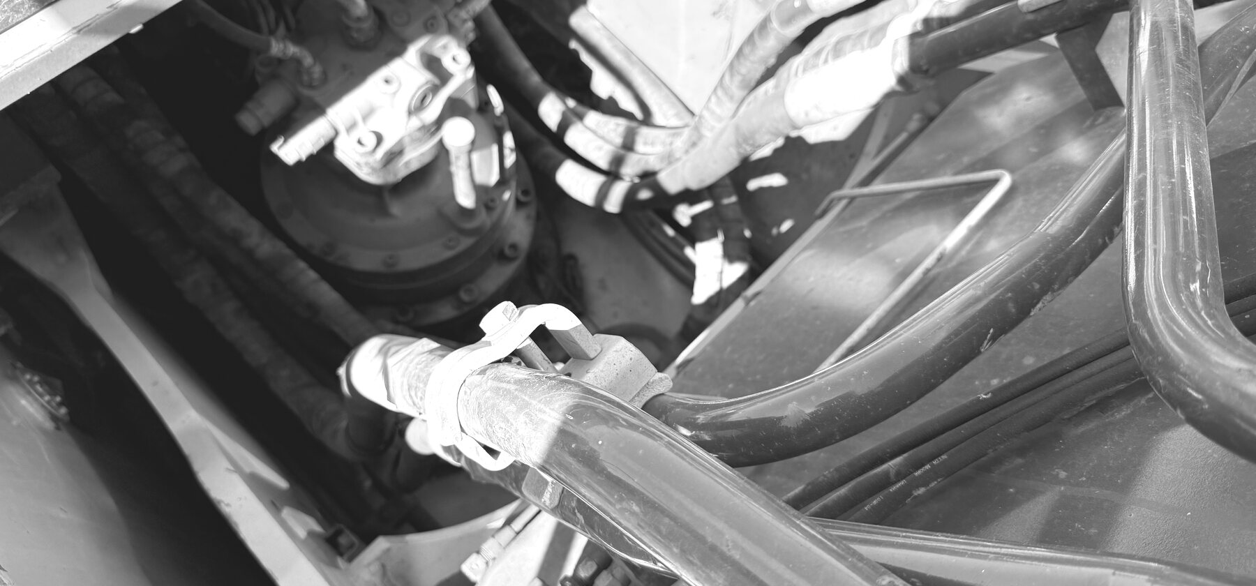 A hydraulic pump and valve block with hoses in an excavator engine bay