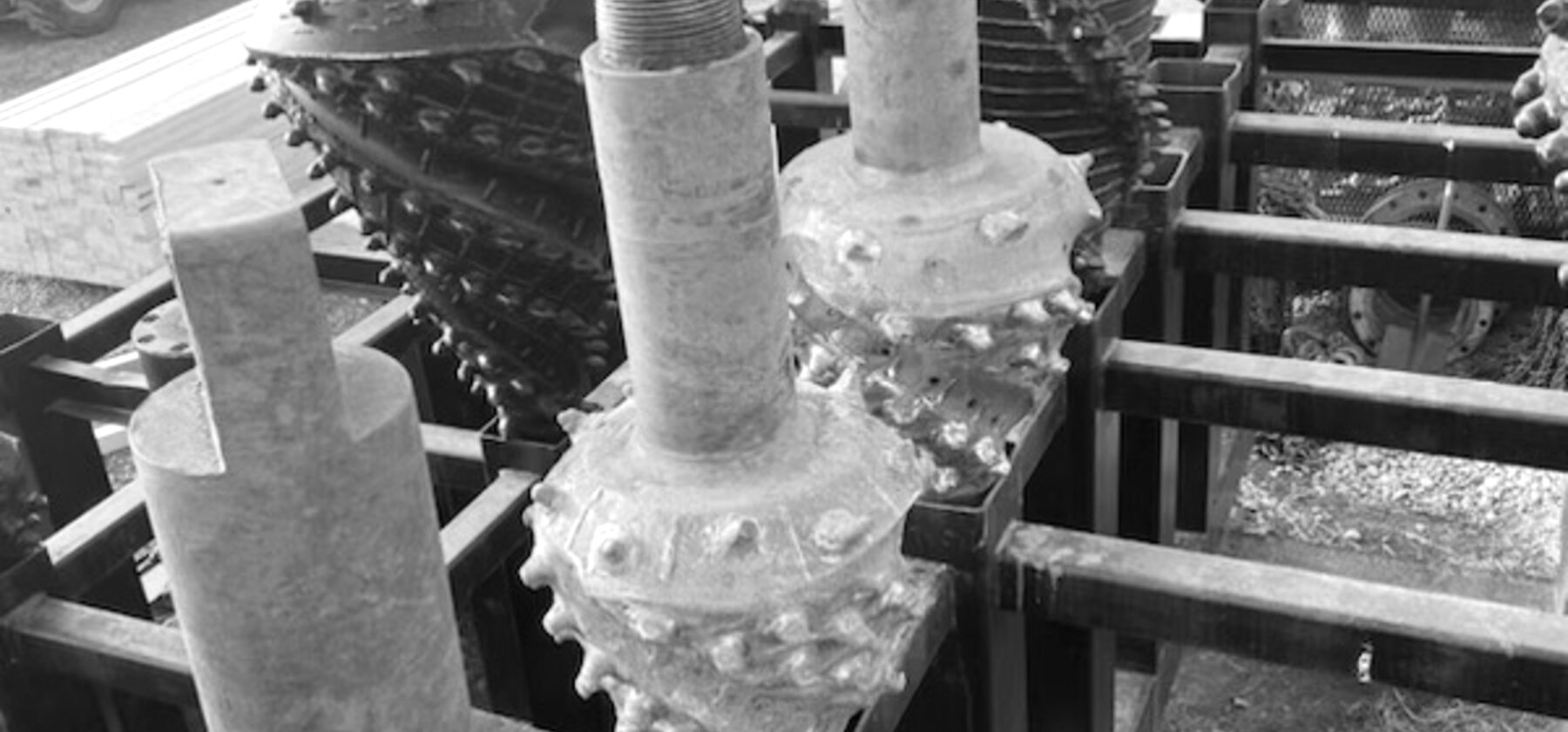 Hole openers and a rock bit standing in a steel rack, their cutter cones and threaded pins worn bright
