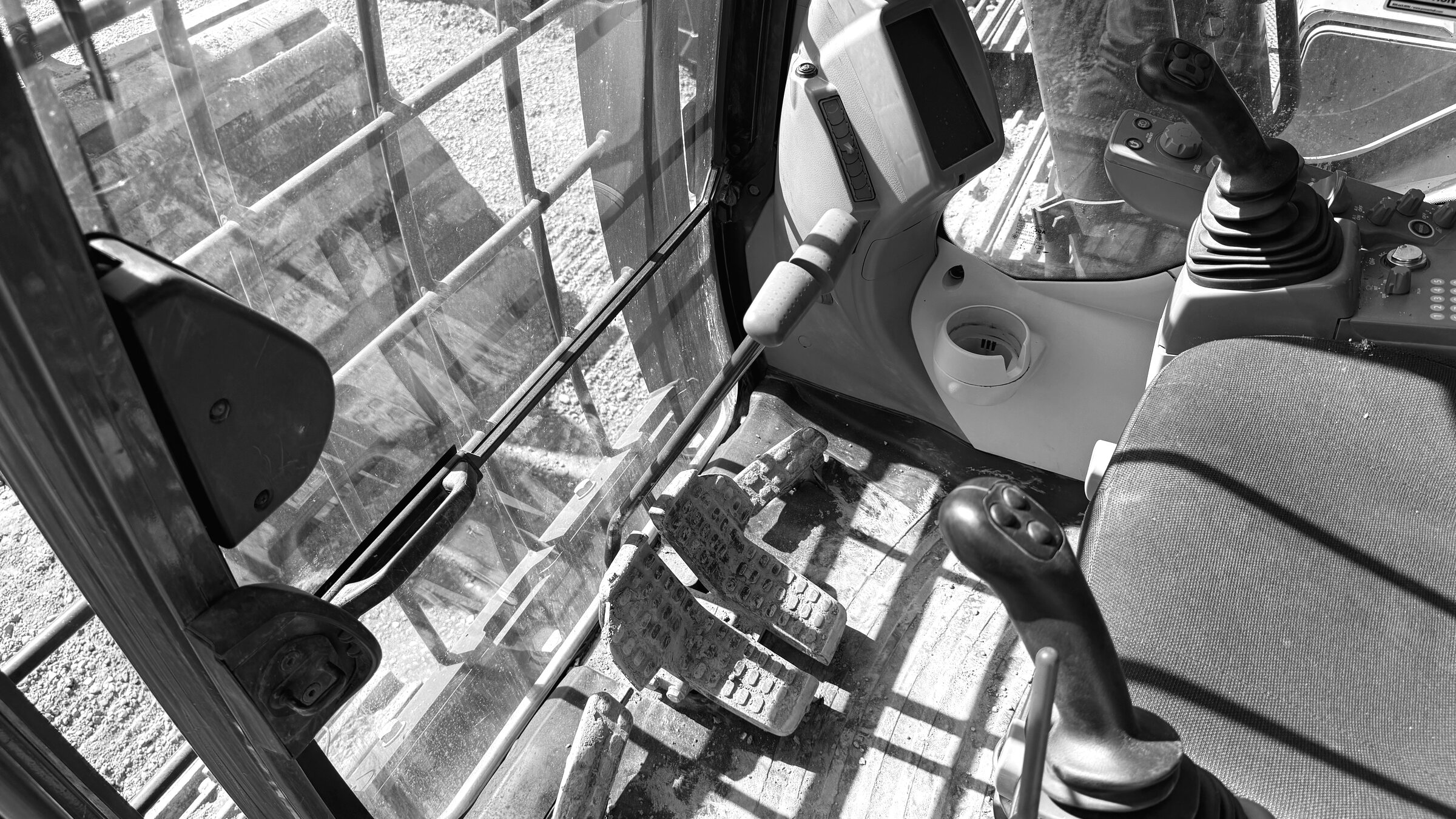 An excavator cab seen through its glass, the control lever and armrest in the foreground