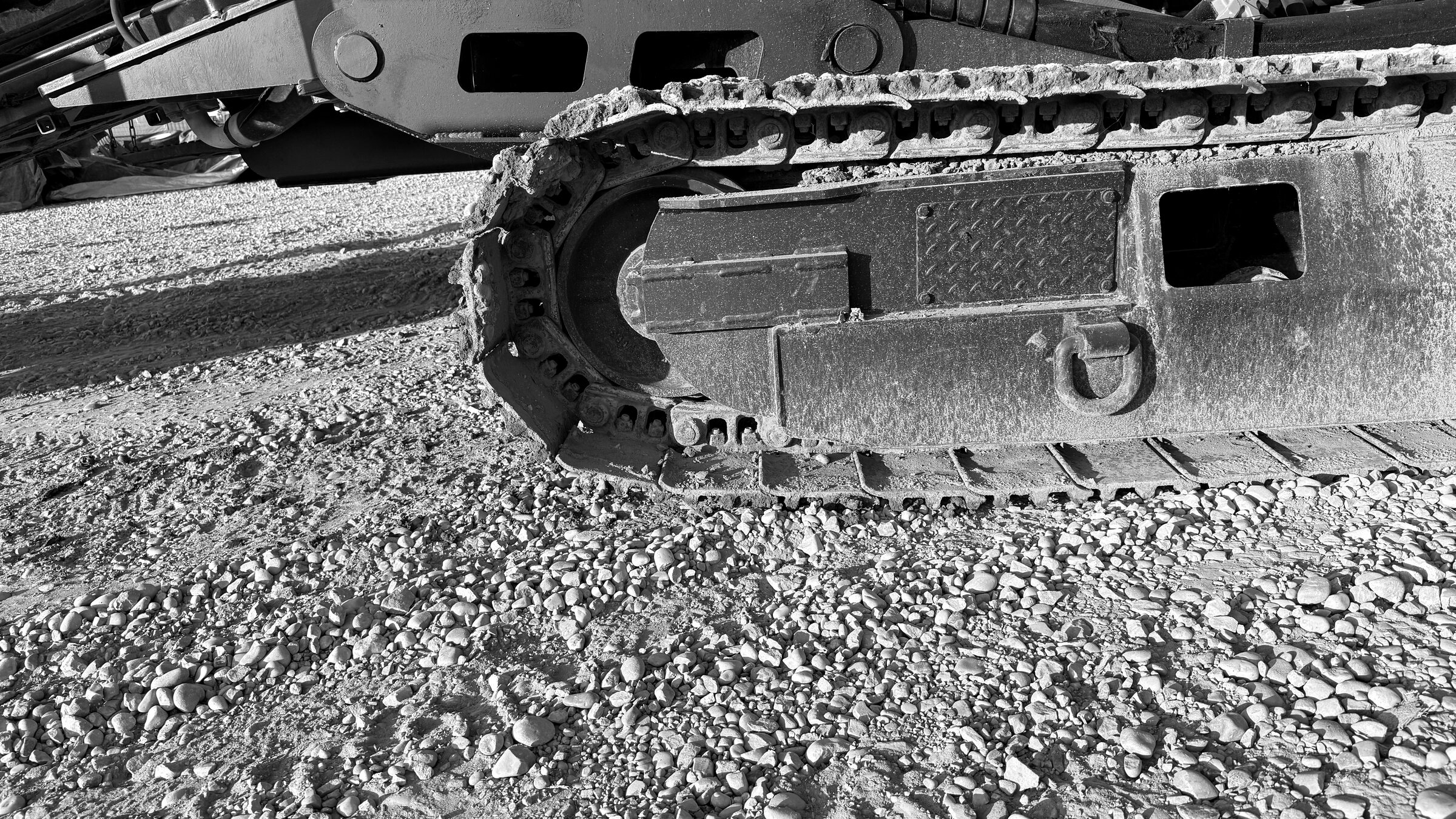 A drill rig's track idler wheel and chain, the undercarriage frame packed with gravel